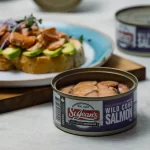 front view of canned smoked wild coho salmon with an open faced sandwich in the background